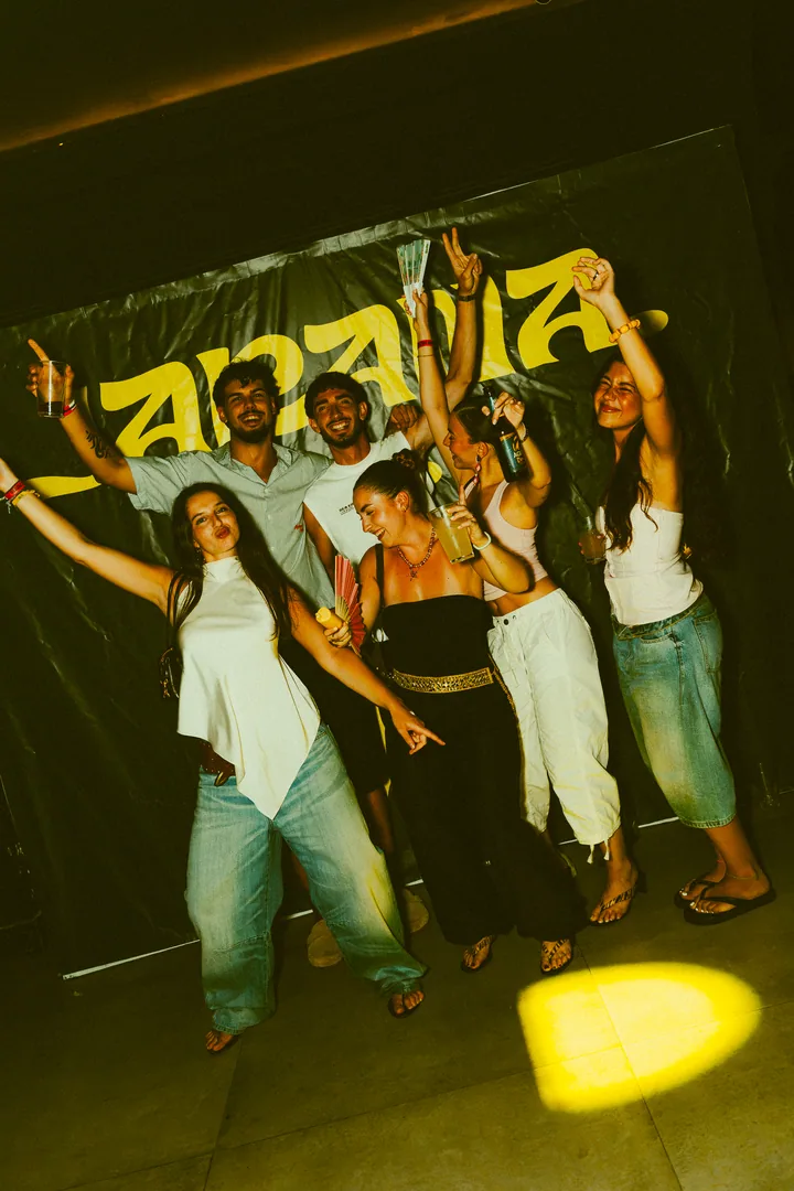 Un grupo de amigos con los brazos en alto delante de la lona de JARANA.