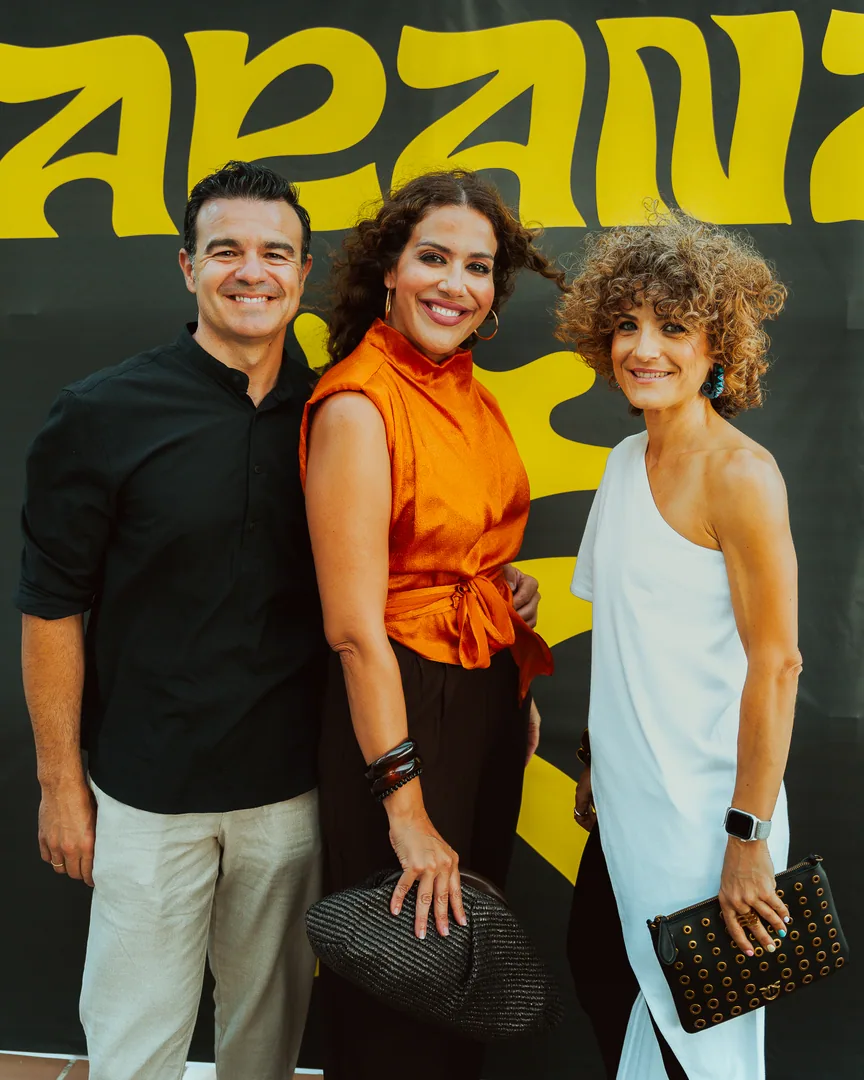 Tres invitados sonríen delante del cartel amarillo de JARANA en El Candelero.