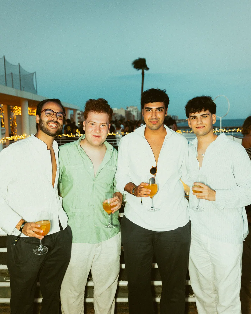 Cuatro chicos con camisa brindan en una terraza junto al mar.